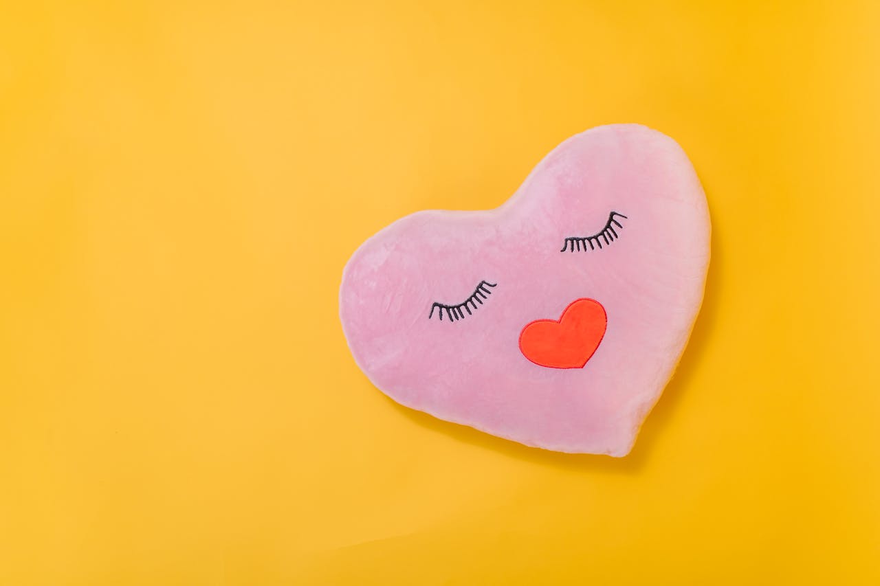 Pink heart-shaped pillow with a cute design on a bright yellow backdrop.
