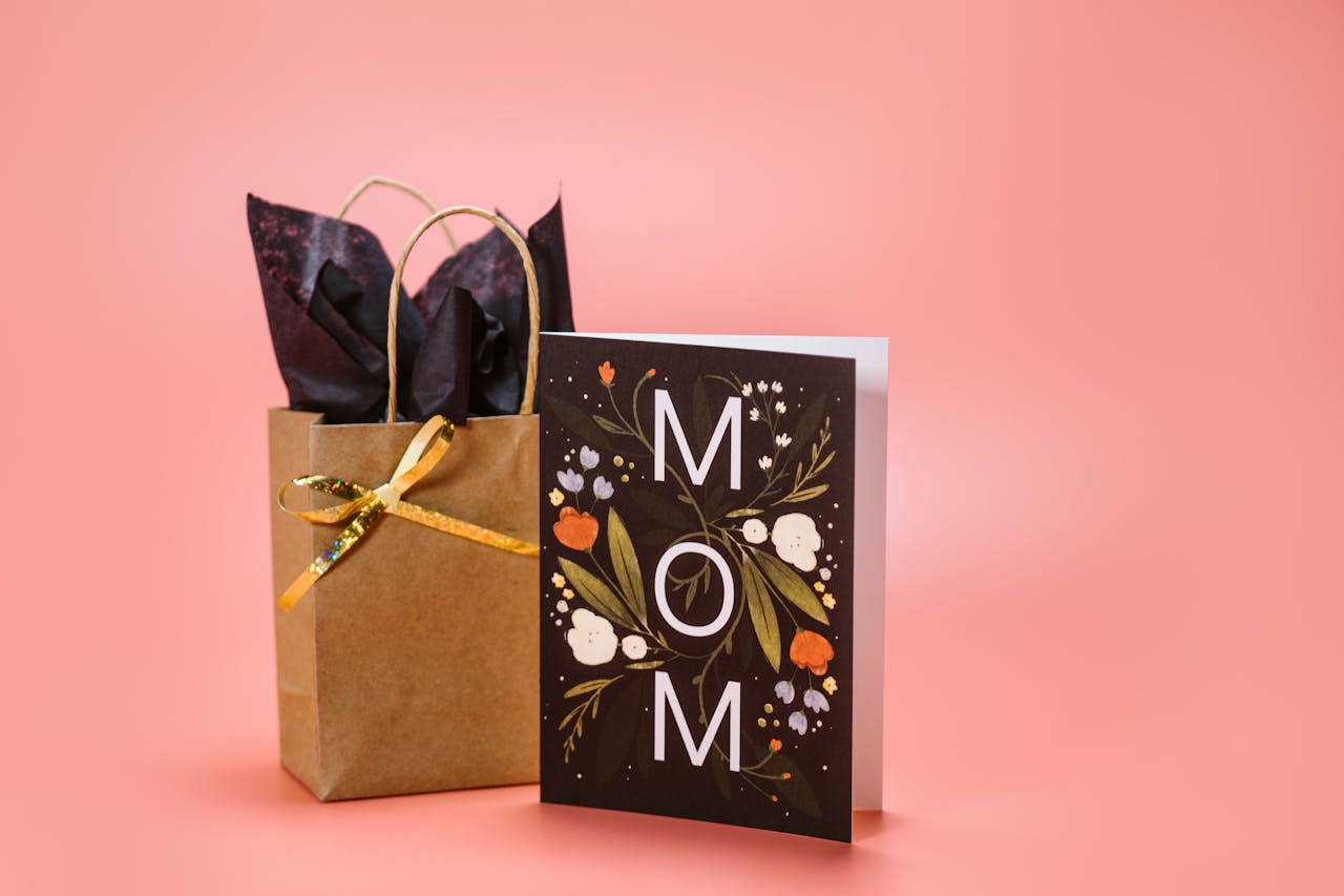 A stylish Mother's Day gift bag and card set with floral design on a pink background.