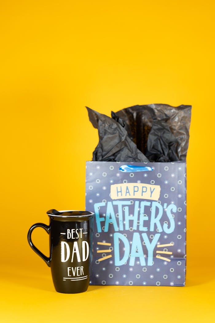 A black mug and gift bag with Father's Day text on a bright yellow background.